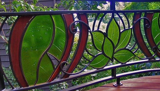 Unique wrought iron handrail design featuring a flower and leaf motif with brown and green stained glass openings for decorative deck railing design.