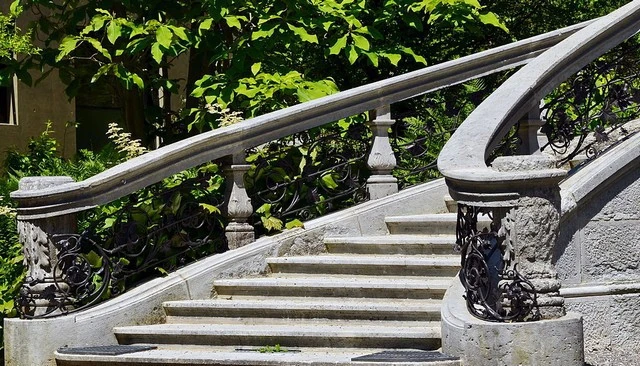 Grand stair railing design featuring a combination of stone and wrought iron, with ornate Grecian urn style newel posts and stone volutes for elegant deck railing design.
