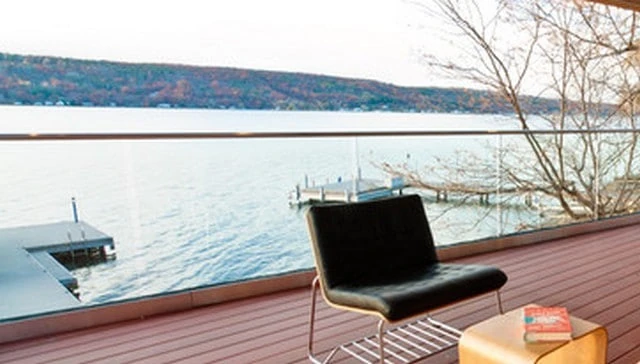 Floating glass panel guardrail featuring a long run of panels without supporting posts, capped by a horizontal wood top for sleek deck railing design.