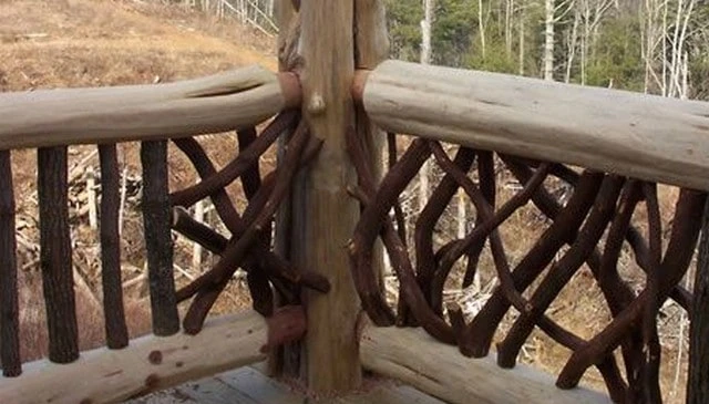 Outdoor handrail design featuring vertical logs with bark and woven branches between log rails, creating a rustic aesthetic for deck railing designs.