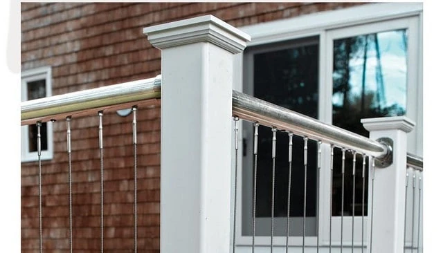 Cable railings mounted between stainless steel pipes with top and bottom installation, featuring white post covers and caps for a modern aesthetic in deck railing designs.