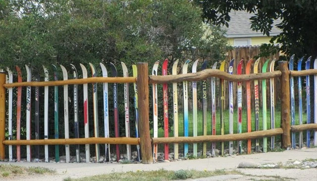 Cross country skis fence featuring a vertical ski collection supported by natural log posts and top and bottom rails, ideal for creative deck railing designs.