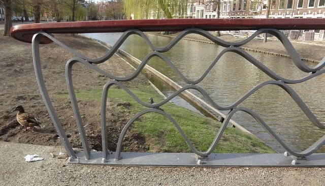 Wavy metal railing design featuring undulating lines that mimic waves, topped with a wood cap for a water-inspired aesthetic.