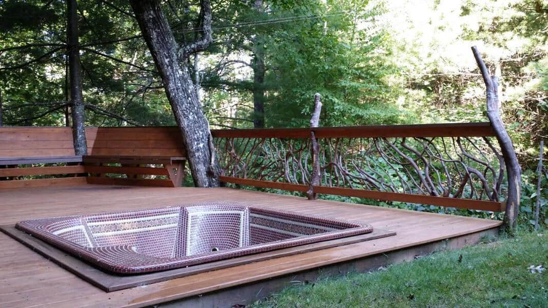 Mountain laurel handrails on a deck patio with a built-in hot tub and a forest background