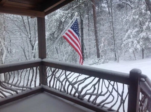 Mountain laurel branch handrails covered in snow with an American flag in a scenic winter setting.