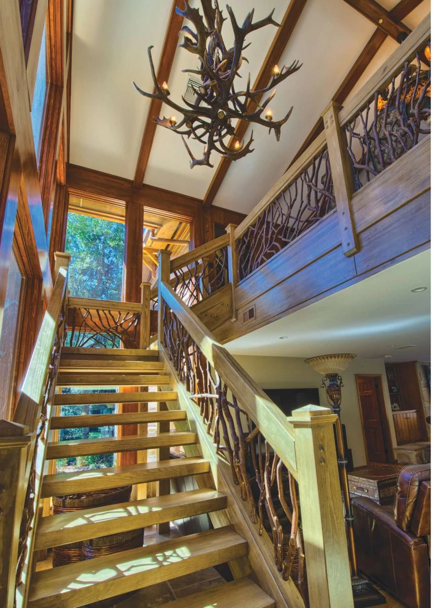 Modern indoor stairs featuring elegant mountain laurel handrails and a rustic antler chandelier, creating a unique and inviting atmosphere.