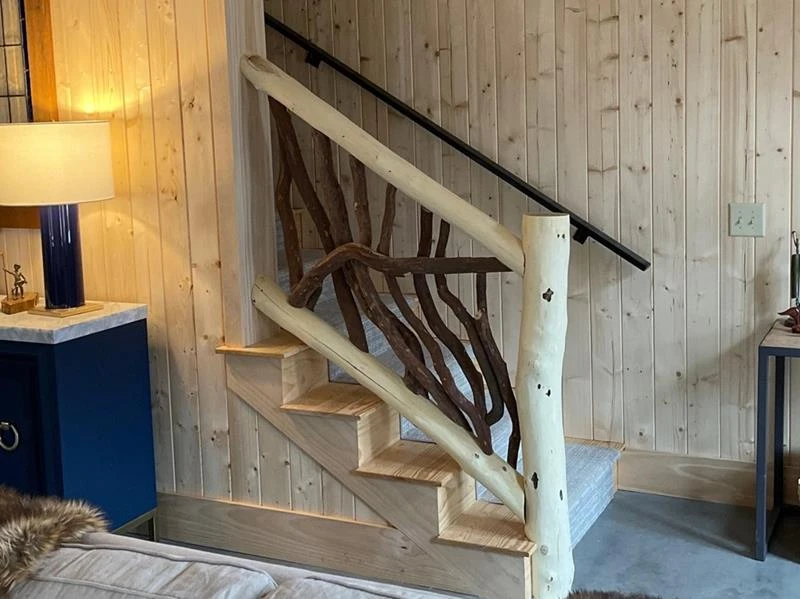 A locust log stair railing featuring bark on full branch posts, designed to enhance safety and add rustic charm to staircases.