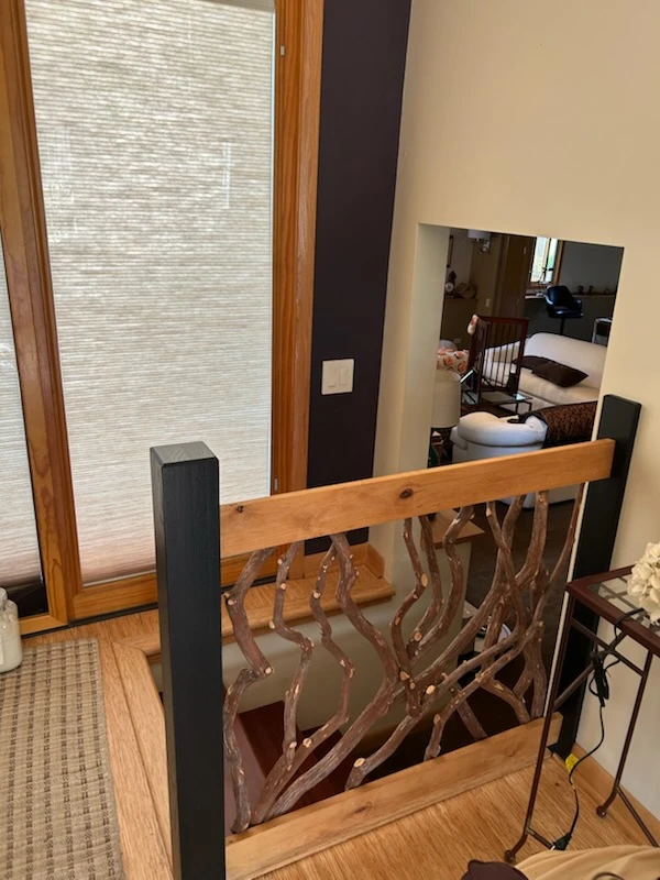 Wood-framed window with shade beside a custom branch-style railing overlooking a downstairs living area.