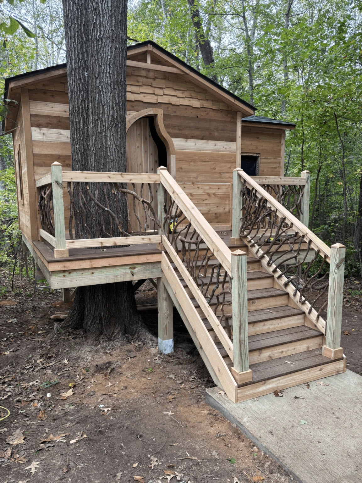 Treehouse Cabin with Branch Railings Wooden treehouse cabin with staircase and woven branch railings built around a large tree.