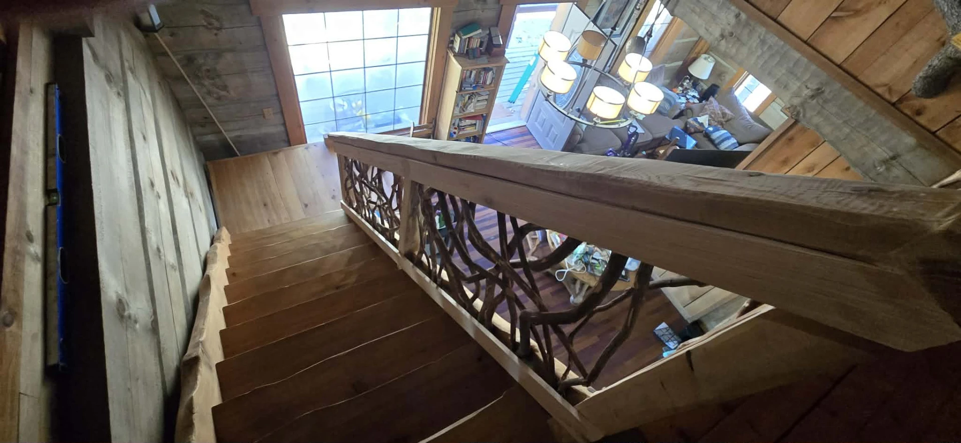 Rustic wooden staircase with woven branch railing inside a log cabin.