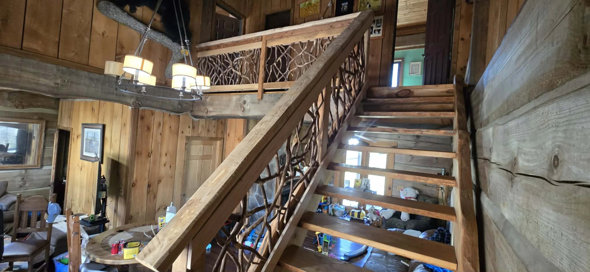 Wide view of a log cabin with a wooden staircase and woven branch railing.