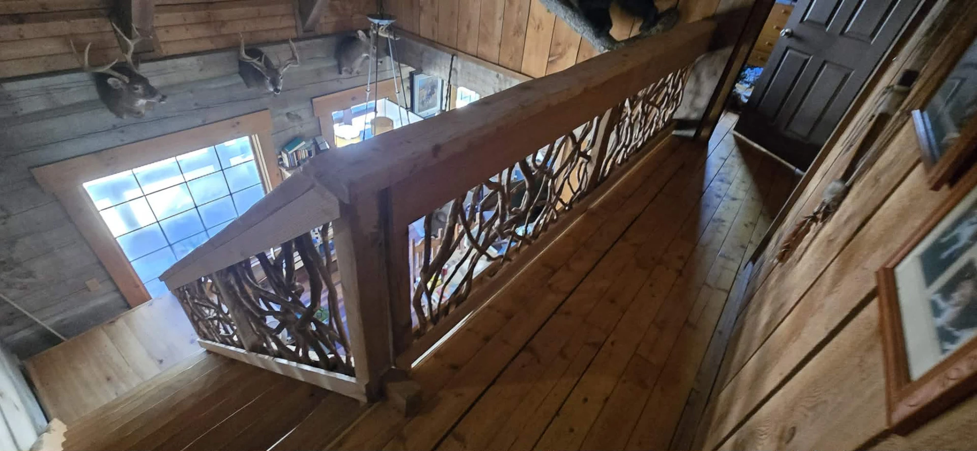 Rustic loft railing with woven branch design overlooking a log cabin interior.