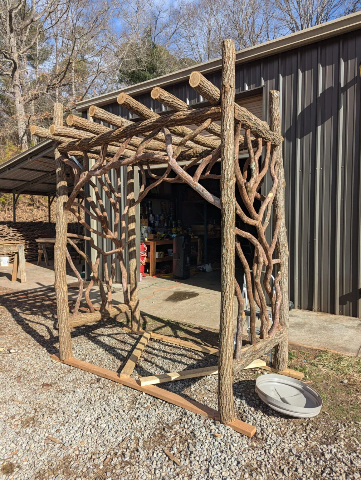 Outdoor pergola frame with woven branch panels and log posts.