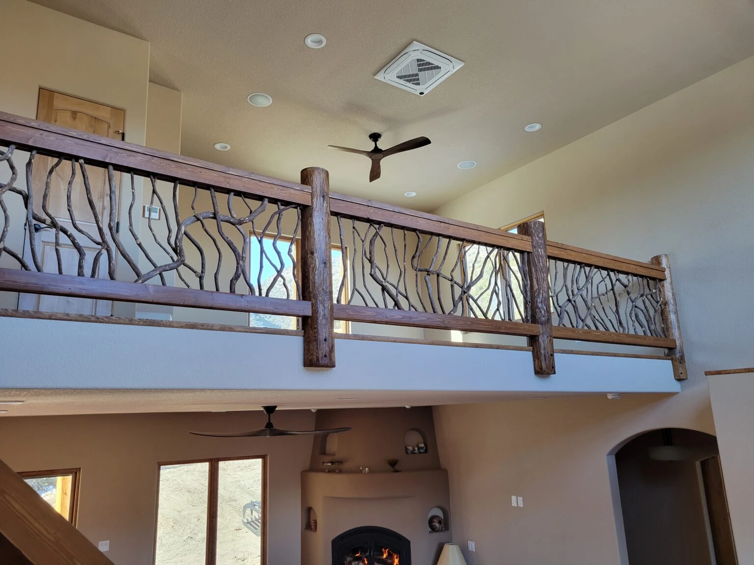 Two-story home interior with rustic wooden balcony railing featuring woven branch design.