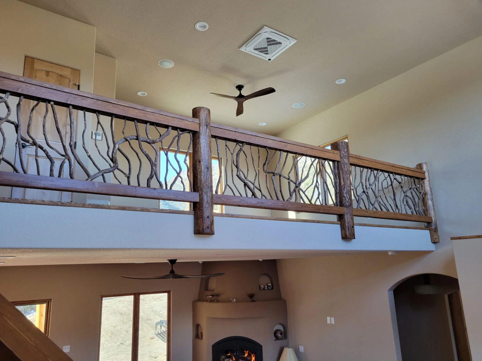 Two-story home interior with rustic wooden balcony railing featuring woven branch design.
