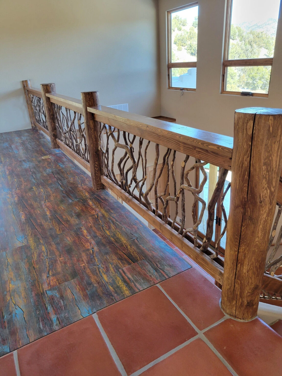 Rustic wooden balcony railing with woven branch design overlooking colorful wood flooring and terracotta tiles.