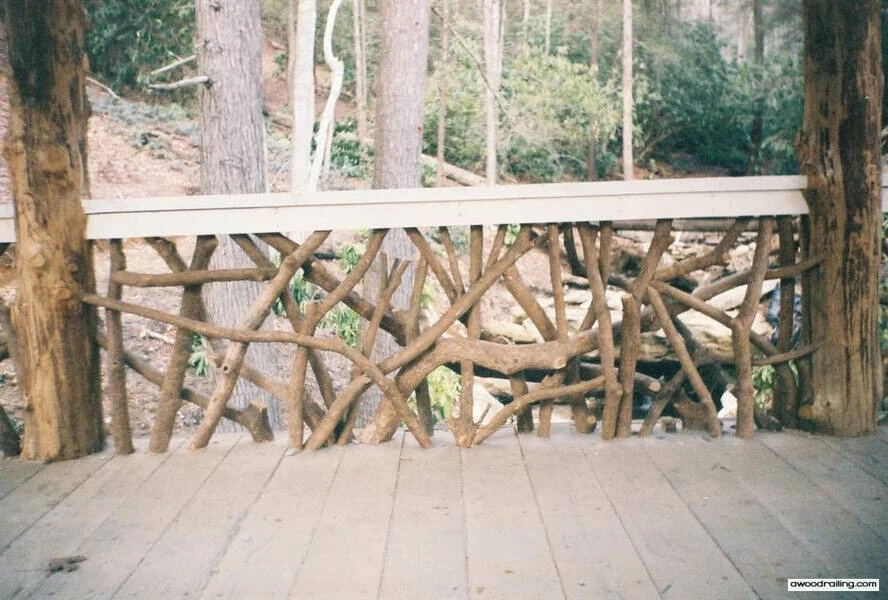 Wooden deck with dense handcrafted woven branch railing made of natural twigs and branches, set against a forest backdrop with tall trees.